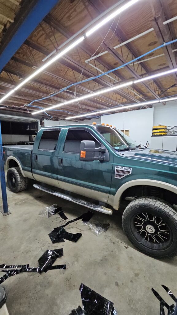 T'S Window Tinting Applying Window Film To A Green Truck With Black Cut Pieces On The Floor Around The Vehicle