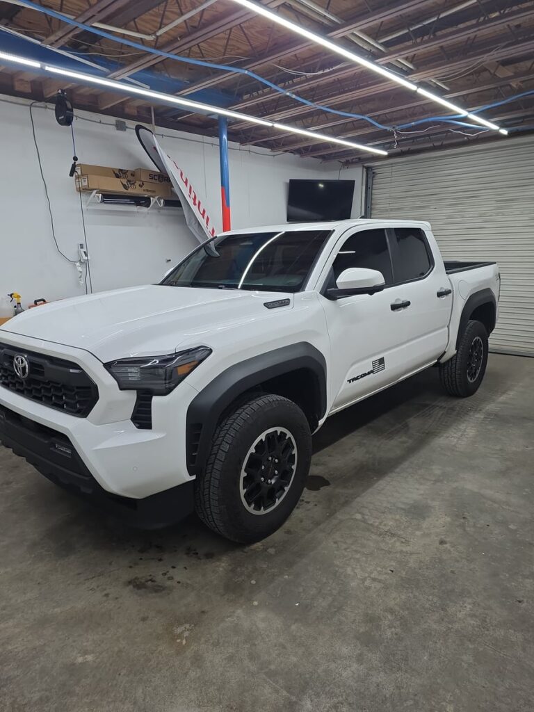 A white Toyota Tacoma pickup sits inside the T’s Window Tinting shop with its freshly tinted windows