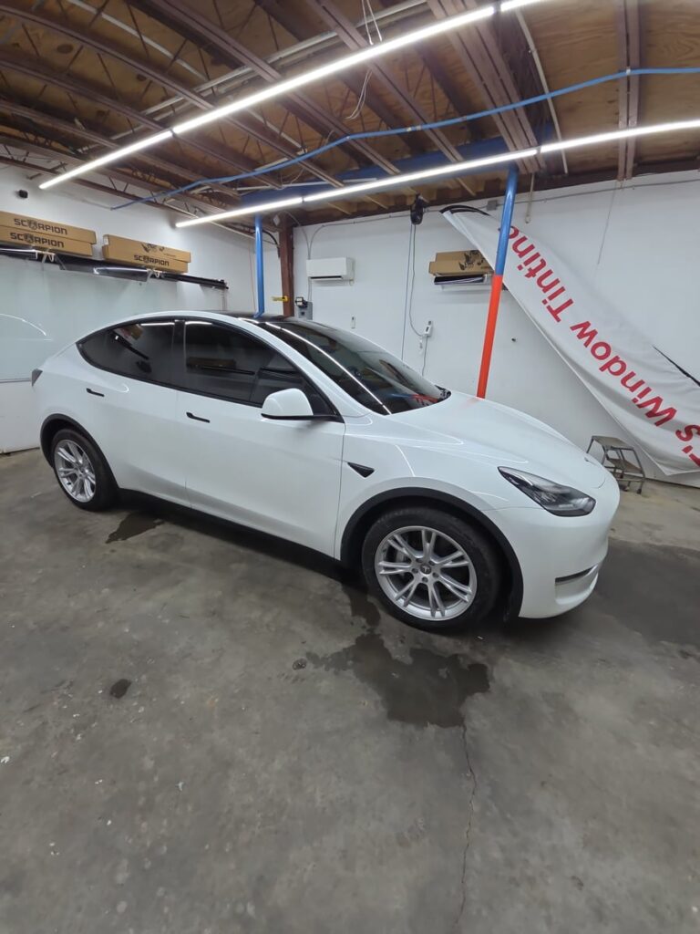 A white Tesla Model Y sits in the T’s Window Tinting shop with freshly tinted windows and a clean, glossy finish