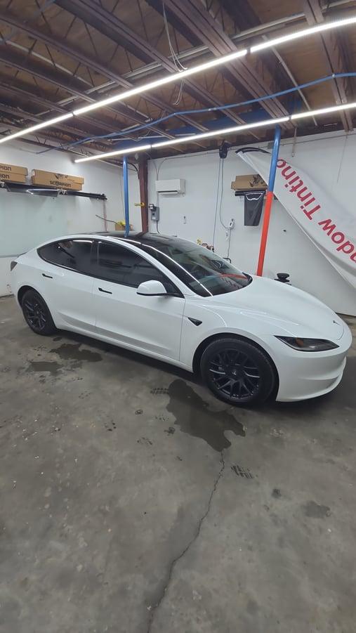 A white Tesla Model 3 with freshly tinted windows is parked inside the T's Window Tinting shop