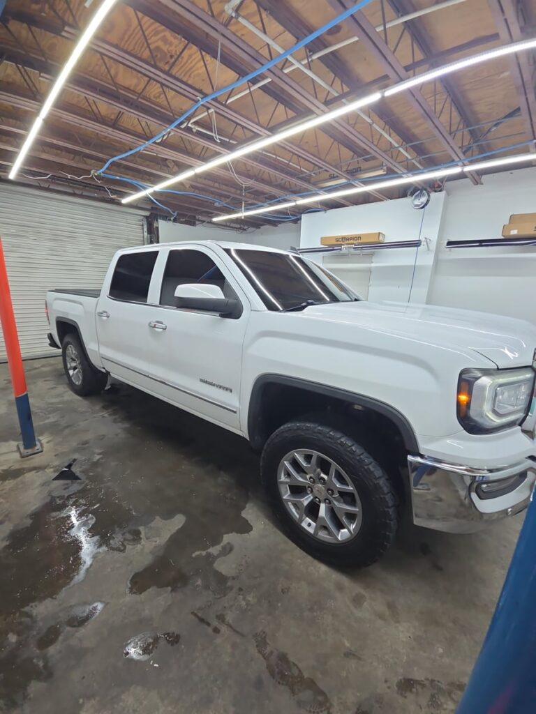A white GMC Sierra pickup sits inside the shop with freshly tinted windows, showcasing the dark, sleek finish from T's Window Tinting