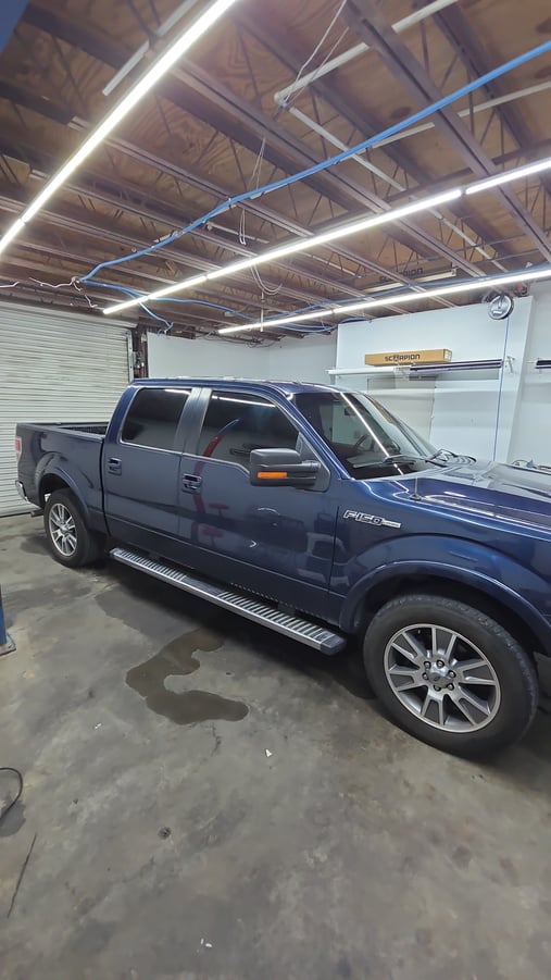 A blue Ford F-150 pickup sits in the shop with freshly tinted windows, showcasing dark, even film on all the side glass
