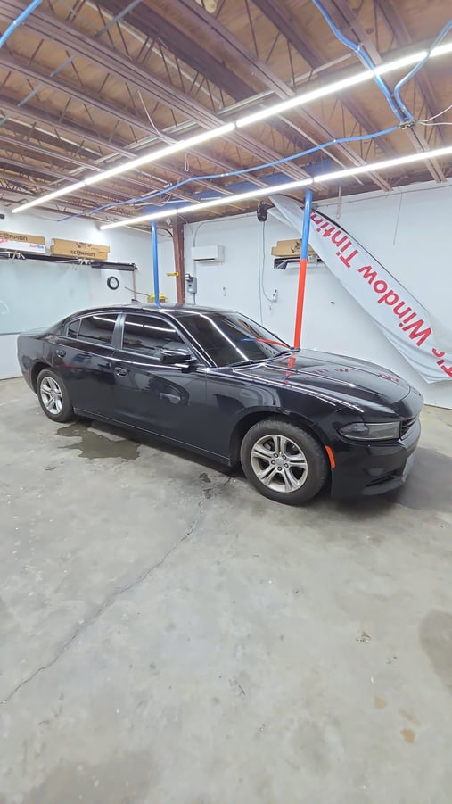A black Dodge Charger sits inside the T's Window Tinting shop with freshly installed dark window tint on all the side and rear windows